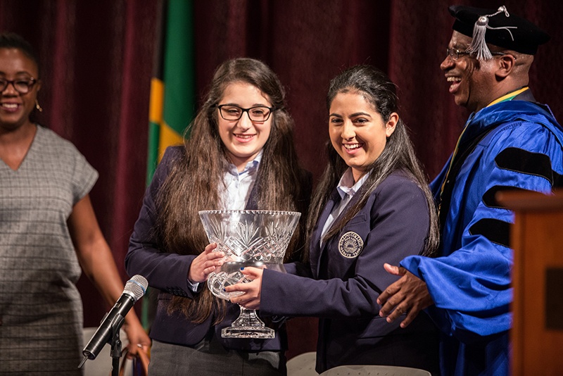 Two female students hold a trophy after winning a debate competition.
