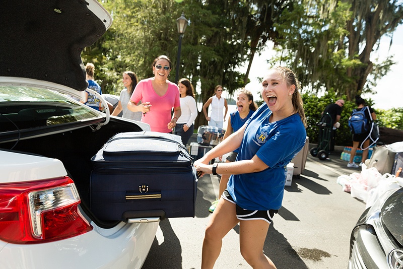Smiling students help a freshmen move into their dorm rooms.