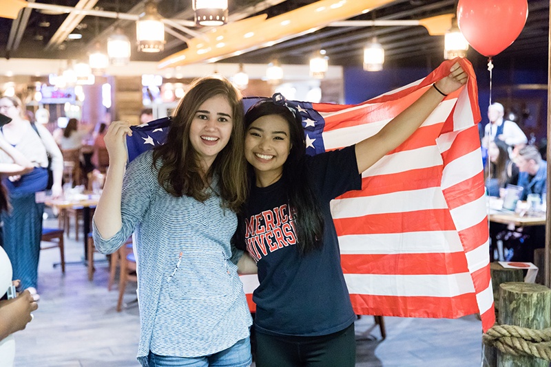 Two students pose with an American flag while monitoring election day results.